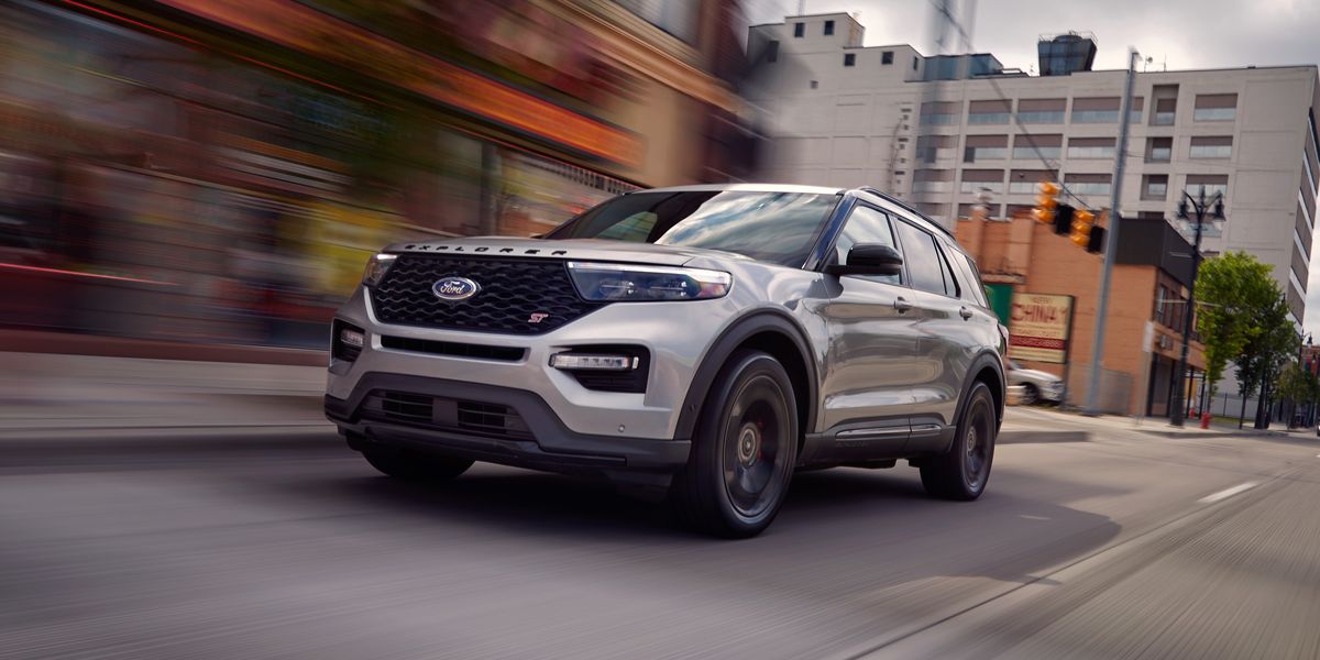 A white suv driving down the street near some buildings.