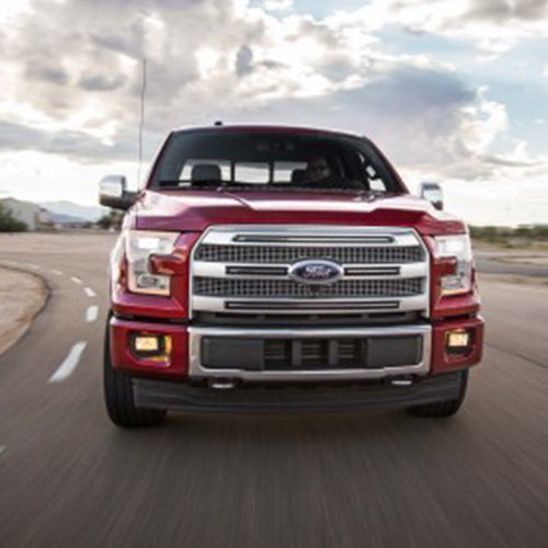 A red truck driving down the road under cloudy skies.