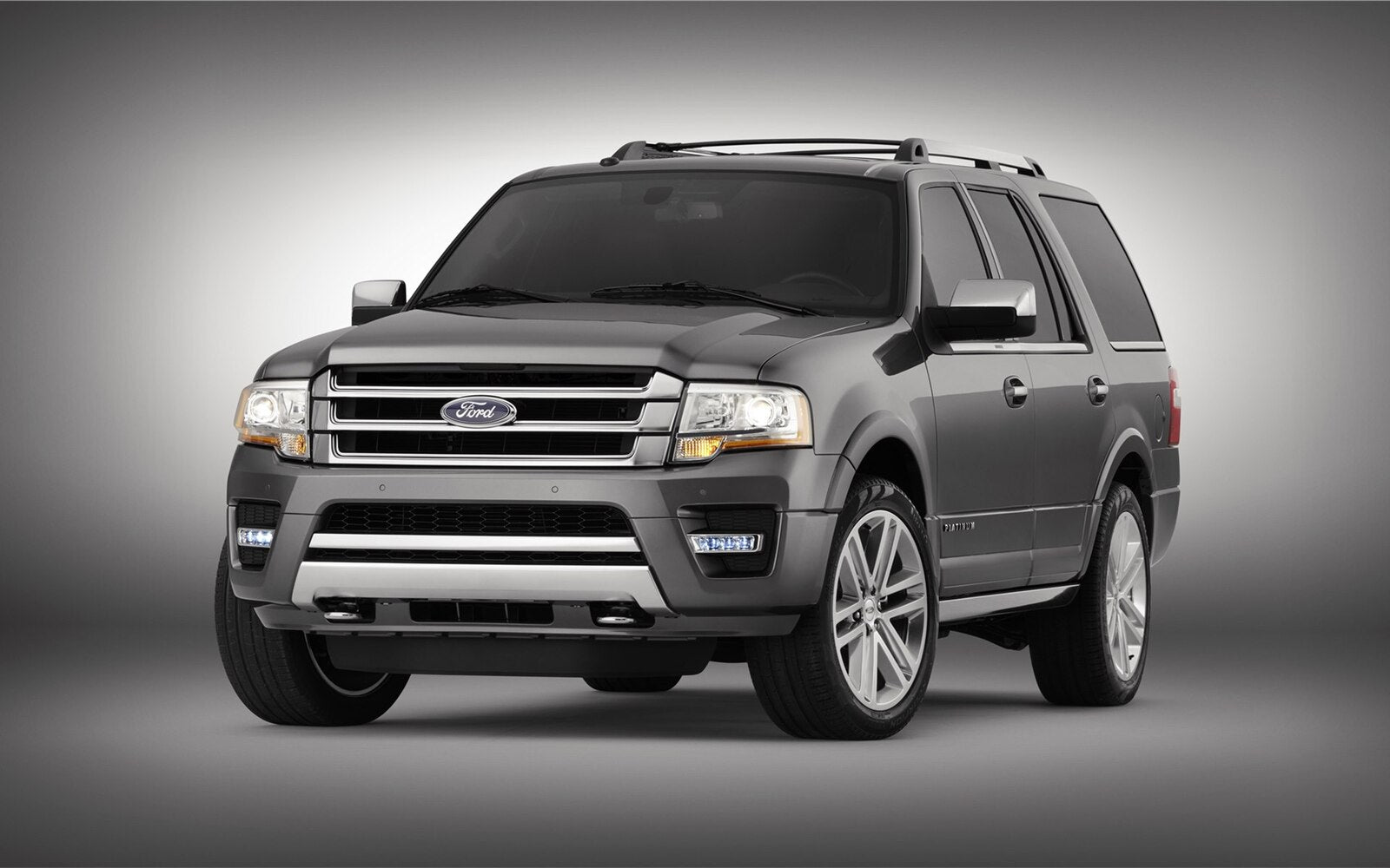 A gray ford expedition is parked in front of a grey background.